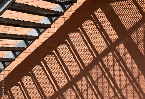 Close up concrete stairs with shading. Architectural details are a brick wall and a metal fire escape. The reflection of the stairs on the brick wall in the sunlight. Geometric shadow pattern. 