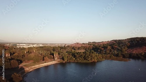 gorgeous footage of a vast rippling blue lake at sunset surrounded by majestic mountain ranges covered in lush green trees and plants with blue sky at Puddingstone Lake in San Dimas California USA photo