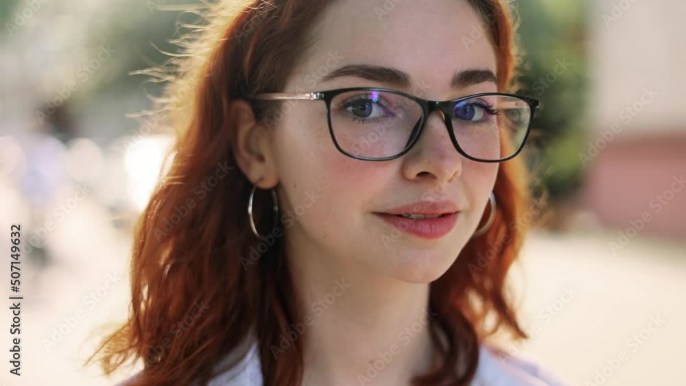 Portrait of attractive red haired woman in eyeglasses while standing in the city street. Beautiful ginger woman looking at the camera outside. High quality 4k footage Portrait of attractive red haired woman in eyeglasses while standing in the city street. Beautiful ginger woman looking at the camera outside. High quality 4k footage