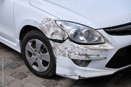 Dented car with damaged fender parked on city street side. Road safety and vehicle insurance concept © bilanol
