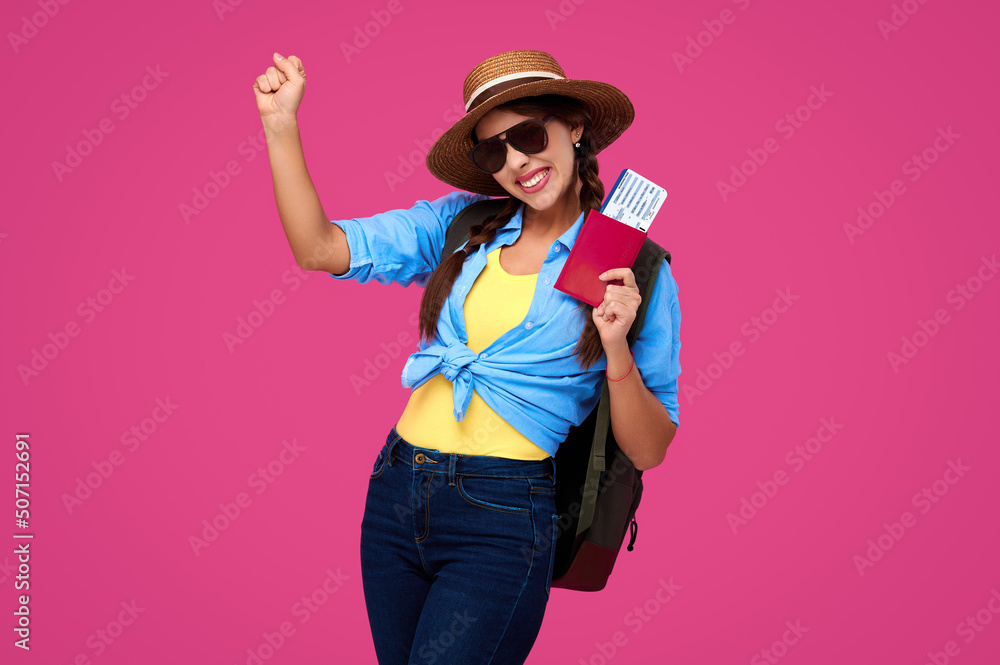Amazed and smiling woman traveler in straw hat and sunglasses holding plane ticket and passport on pink isolated background Amazed and smiling woman traveler in straw hat and sunglasses holding plane ticket and passport on pink isolated background