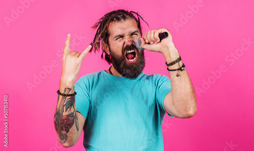 Bearded man singing in microphone with horns gesture heavy metal rock. Hipster enjoying karaoke. photo