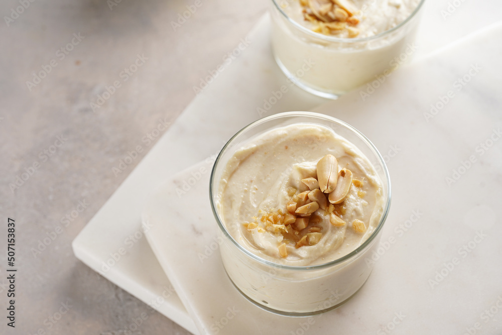 Creamy dairy yoghurt dessert with mascarpone, cream cheese and peanut butter in glasses on marble tray with a tea spoon Creamy dairy yoghurt dessert with mascarpone, cream cheese and peanut butter in glasses on marble tray with a tea spoon