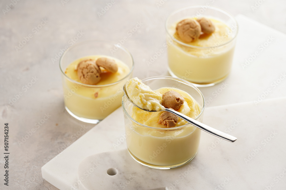 Creamy french vanilla pudding in glass decorated with italian biscuits amaretti on marble board on grey neutral background Creamy french vanilla pudding in glass decorated with italian biscuits amaretti on marble board on grey neutral background