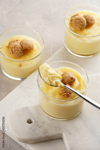 Creamy french vanilla pudding in glass decorated with italian biscuits amaretti on marble board on grey neutral background