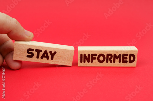 On a red background, wooden blocks, one of them in hand. The blocks are written - STAY INFORMED