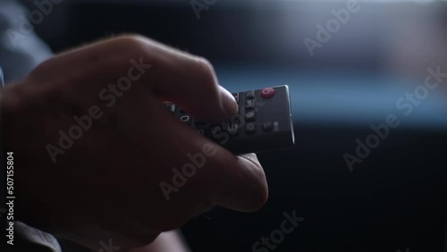 Close-up unrecognizable mature adult male hands holding TV remote control and switches TV channel. Closeup cropped shot of senior man flipping through TV channels with remote control, slow motion. photo