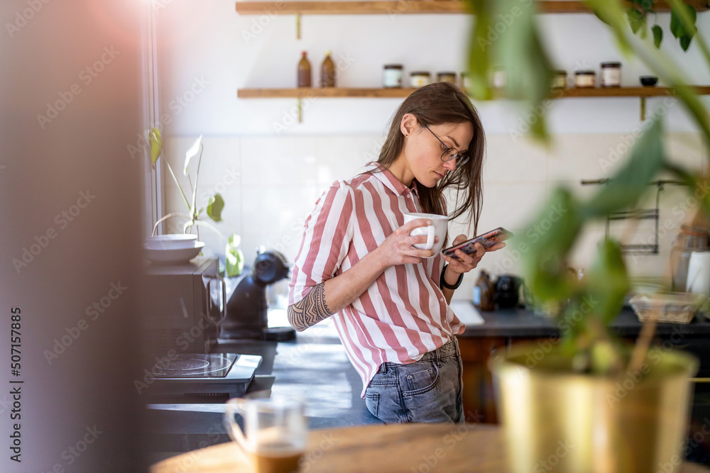 Young woman using smartphone while standing in her kitchen at home
Young woman using smartphone while standing in her kitchen at home