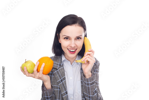 smiling woman in office suit holding an apple and an orange in one hand, calling a banana with the other hand, healthy fruit snack, white studio background. High quality photo