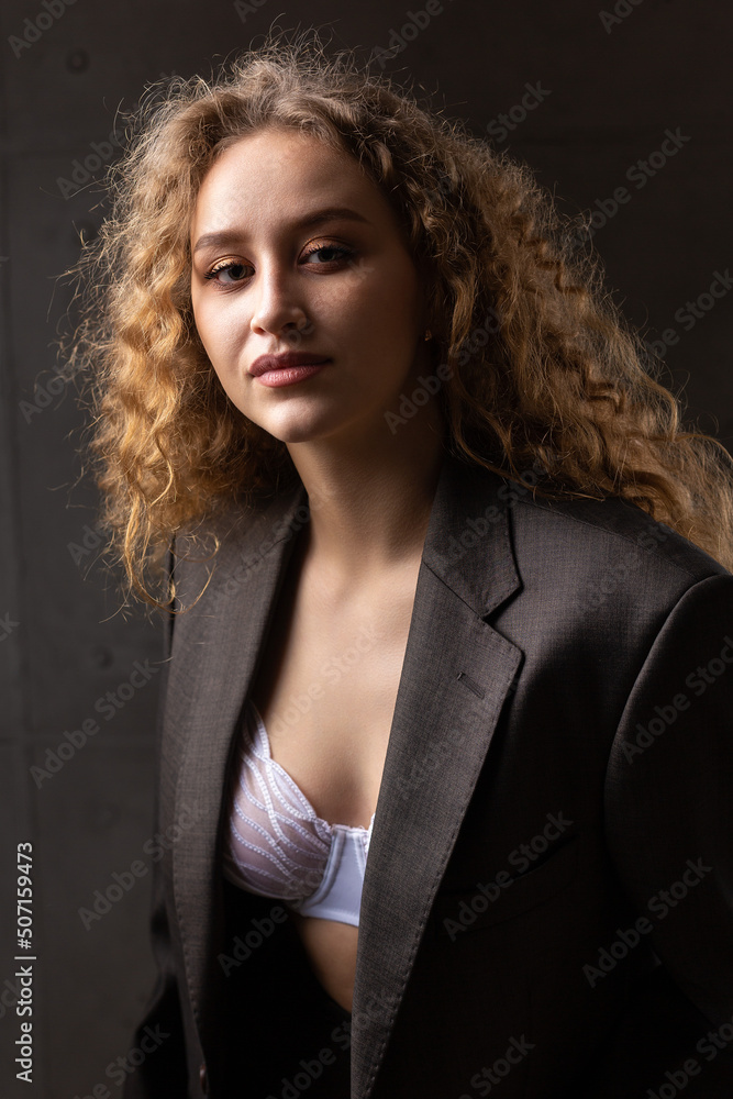 Portrait of a young red-haired curly sexy girl in a jacket with long hair in the studio. Shows off her curvaceous breasts in a bra. Portrait of a young red-haired curly sexy girl in a jacket with long hair in the studio. Shows off her curvaceous breasts in a bra.