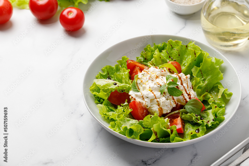 Green Salad with stracciatella cheese, lettuce leaves, tomatoes, and sauce.  Keto diet, healthy and detox food concept. Vegetable salad bowl.