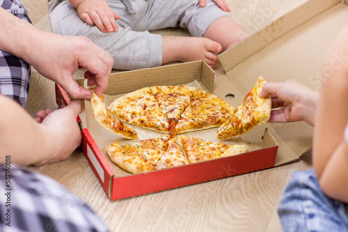 Family hands taking pizza slices on wooden floor background.