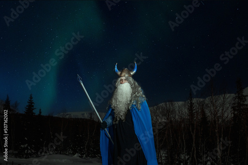 Photos old man Odin with a staff stands in the snow at night against the backdrop of th