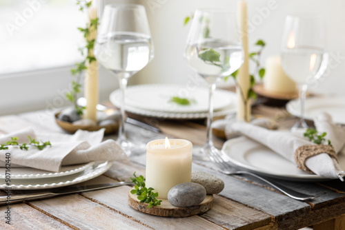 Rustic zero waste wedding decor with natural elements. Wooden table, candles, linen napkins, branches with green leaves. Eco-friendly decoration for the special dinner. Romantic and cozy place