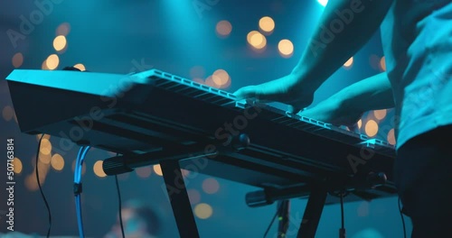 Close up view of musician hand playing synthesizer piano on live concert at stage. The musician playing the electric piano. Blue background