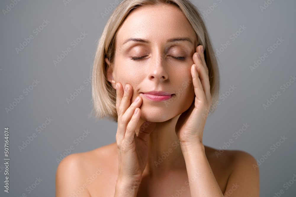 Skin care. Blonde woman with beauty face touching healthy facial skin. No makeup. Grey background. Skin care. Blonde woman with beauty face touching healthy facial skin. No makeup. Grey background.