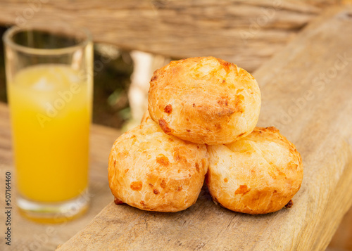 Delicious Minas cheese bread, on a rustic wooden bench, outdoors, with a glass of orange juice in the background photo