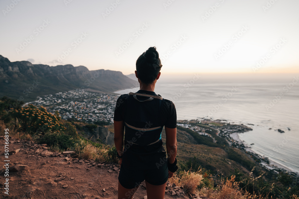 Rear view of sportswoman on the mountain taking a break after running at sunset. Female runner relaxing on a mountain enjoying the view.