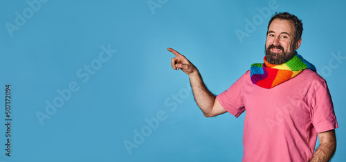 pride day. lgtb community. happy gay man, pointing to a large empty space for advertising. lgtb flag on scarf.