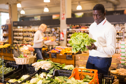 African American man shopping in organic food store, choosing fresh vegetables