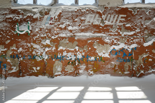 The interior of a sports hall in an abandoned school in the Arctic. Snow on the floor. On the wall is peeling paint and the text in Russian 