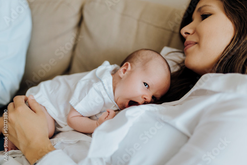 Happy newborn baby boy yawning on top of his mother lying on the sofa