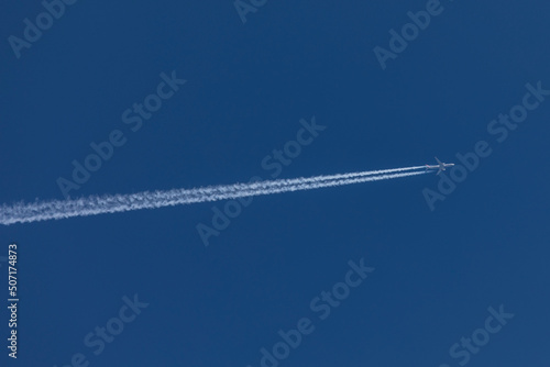 aviation, travel by airplane, bright blue sky on a sunny day without clouds, an airplane is flying from the left to the right and leaves a large jet stream behind