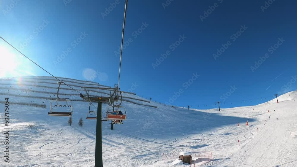 Fast forward effect first-person view FPV point of view POV of cable chair ski lift ascend for alpine skiing. Ski resort piste with people skiing in Dolomites. Ski area Belvedere. Canazei, Italy Fast forward effect first-person view FPV point of view POV of cable chair ski lift ascend for alpine skiing. Ski resort piste with people skiing in Dolomites. Ski area Belvedere. Canazei, Italy