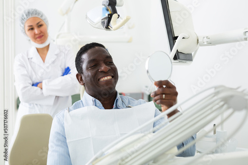 Smiling adult african american man sitting in chair in dental office, satisfied with result of teeth treatment..