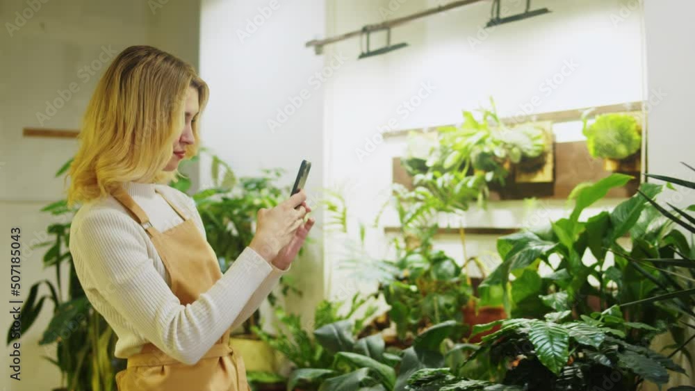Florist taking photo of flowers. Woman gardener using phone camera, making photos of blooming houseplant, flower shop. Botanist greenhouse worker. Florist taking photo of flowers. Woman gardener using phone camera, making photos of blooming houseplant, flower shop. Botanist greenhouse worker.