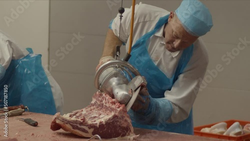 Butcher using electric saw to cut piece of meat photo