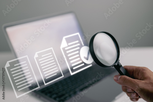 Documents and magnifying glass. Confirmed or approved document on laptop computer. photo