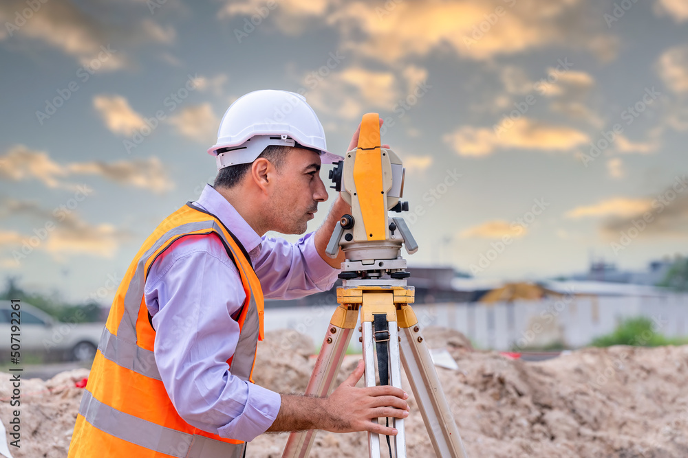 Surveyor engineer wearing safety uniform and helmet with equipment theodolite to measurement positioning on the construction site of the road with construct machinery background Surveyor engineer wearing safety uniform and helmet with equipment theodolite to measurement positioning on the construction site of the road with construct machinery background