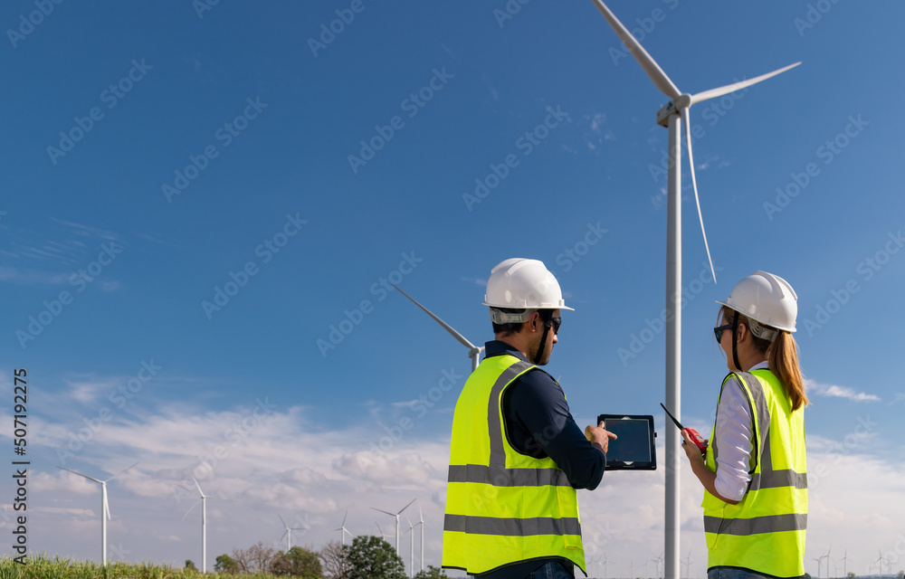 Engineer wearing uniform ,helmet inspection and survey work in wind turbine farms rotation to generate electricity energy. Green ecological power energy generation wind sustainable energy concept. Engineer wearing uniform ,helmet inspection and survey work in wind turbine farms rotation to generate electricity energy. Green ecological power energy generation wind sustainable energy concept.