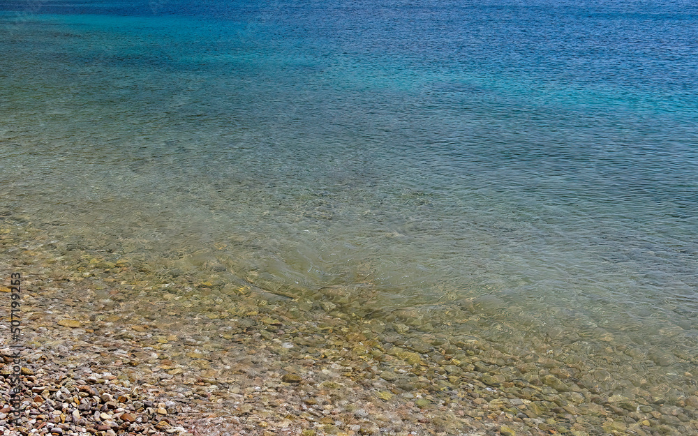 The light ripples of the turquoise sea near a pebble beach. Summer in the Greek islands.