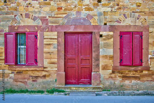 An old stone house front with a red painted wooden door and two windows. Campos, Chios island, Greece. photo