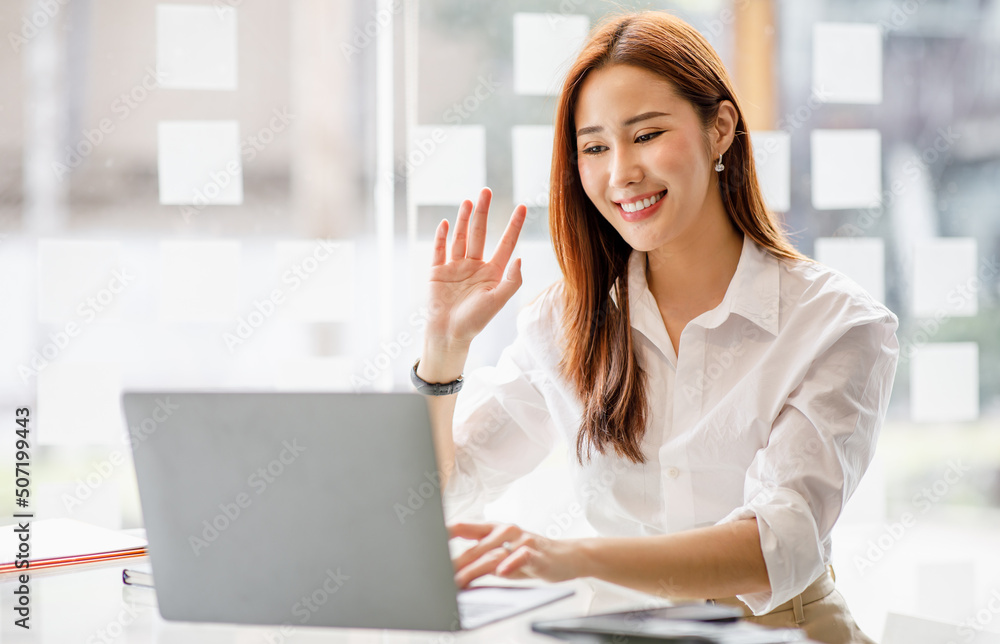 Happy young asian business woman waving hands to greeting partner during making video conference with her team. Happy young asian business woman waving hands to greeting partner during making video conference with her team.