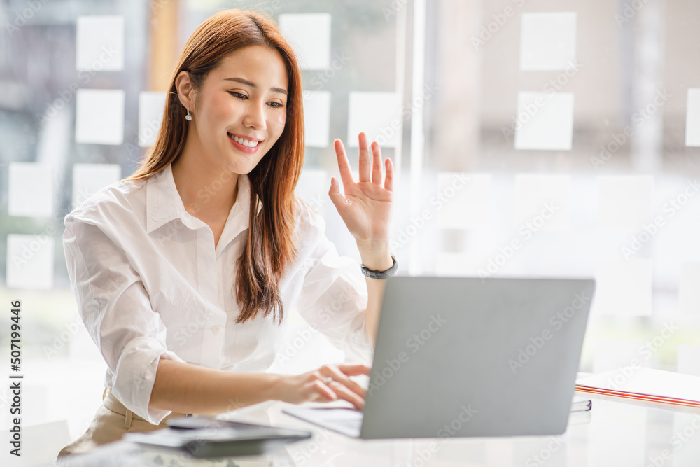 Happy young asian business woman waving hands to greeting partner during making video conference with her team. Happy young asian business woman waving hands to greeting partner during making video conference with her team.