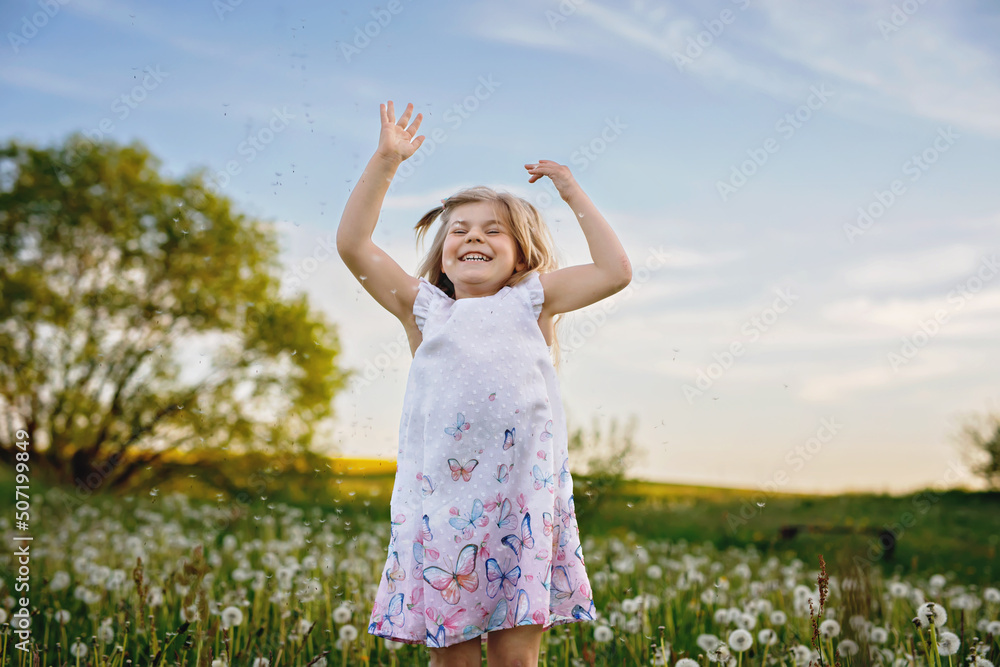 Adorable cute little preschool girl on a dandelion flower on the nature in the summer. Happy healthy beautiful toddler child with flowers, having fun. Bright sunset light, active kid. Adorable cute little preschool girl on a dandelion flower on the nature in the summer. Happy healthy beautiful toddler child with flowers, having fun. Bright sunset light, active kid.
