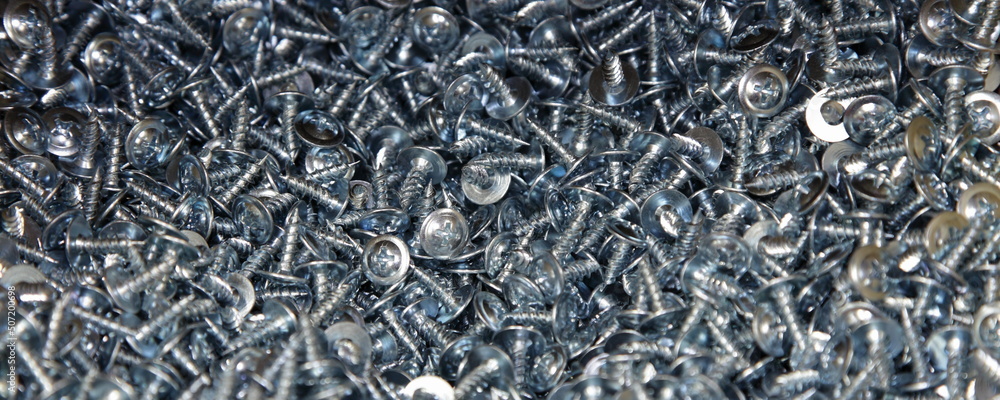 A many new short grey shiny self-tapping screws with cross heads. Galvanized construction fasteners. Industrial wide texture background. A many new short grey shiny self-tapping screws with cross heads. Galvanized construction fasteners. Industrial wide texture background.