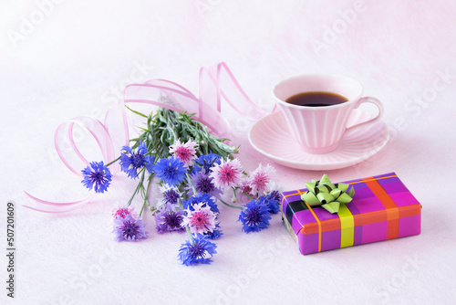 プレゼントとコーヒーとヤグルマギクの花束のデザイン（ピンクのコーヒーカップ、ピンクバック）