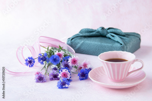 コーヒーとヤグルマギクの花束と風呂敷包みのデザイン（ペールピンクの背景） 
