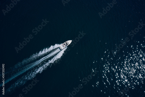 Top view of a white boat sailing to the blue sea. Drone view of a boat sailing.Motor boat in the sea. Travel - image. Large white boat fast movement on blue water aerial view.