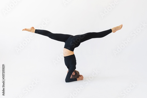 Fotografia Woman in black sportswear practicing yoga doing shirshasana exercises with hanum