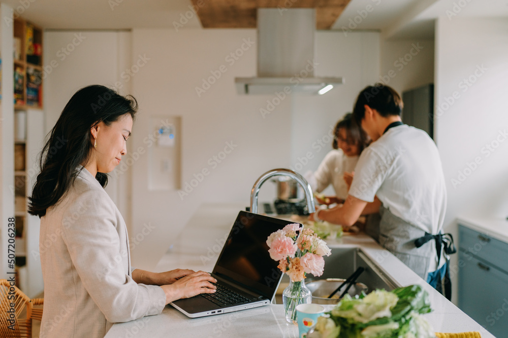 在宅勤務をする母と食事の準備をする父親と娘 在宅勤務をする母と食事の準備をする父親と娘