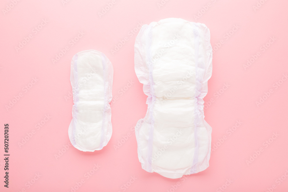 Two new opened white sanitary towels on light pink table background. Big and small size. Pastel color. Closeup. Hygiene product for urinary incontinence or after childbirth. Top down view. Two new opened white sanitary towels on light pink table background. Big and small size. Pastel color. Closeup. Hygiene product for urinary incontinence or after childbirth. Top down view.