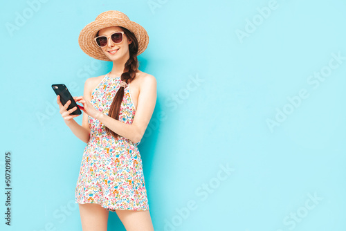 Young beautiful smiling female in trendy summer skirt. Sexy woman with posing near yellow wall in studio. Positive model having fun. In sunglasses and hat.Looking at smartphone. Using apps