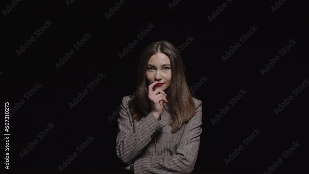 A beautiful young brunette in a jacket looks seductively into the camera on a black background. A beautiful young brunette in a jacket looks seductively into the camera on a black background.