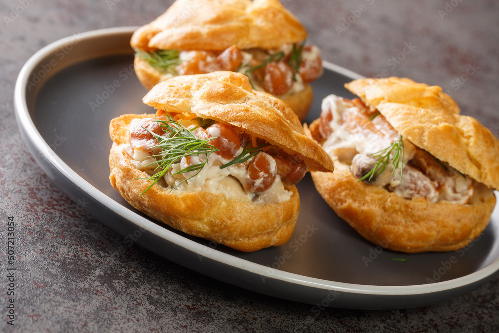 Profiteroles stuffed with stewed mushrooms with creamy sauce and dill close-up in a plate on the table