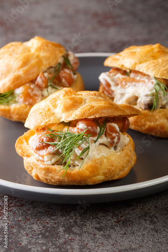 Delicious profiteroles stuffed with mushrooms in a creamy sauce with cheese and herbs close-up in a plate on the table